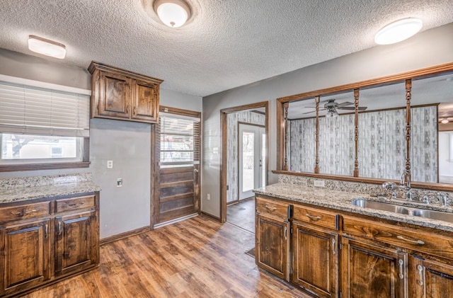 kitchen featuring a sink, baseboards, light wood-style floors, and light stone counters