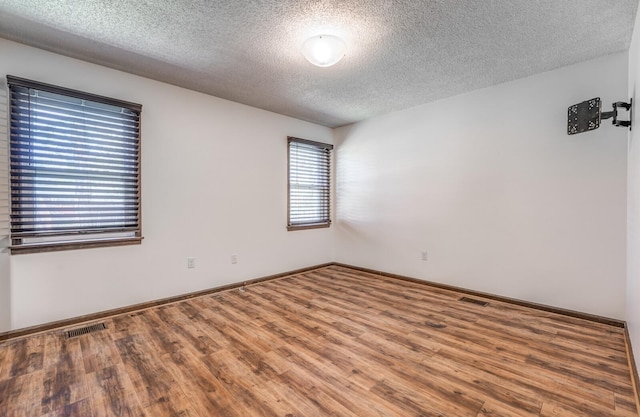 empty room with baseboards, visible vents, wood finished floors, and a textured ceiling