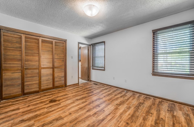 unfurnished bedroom featuring a closet, a textured ceiling, baseboards, and light wood-type flooring