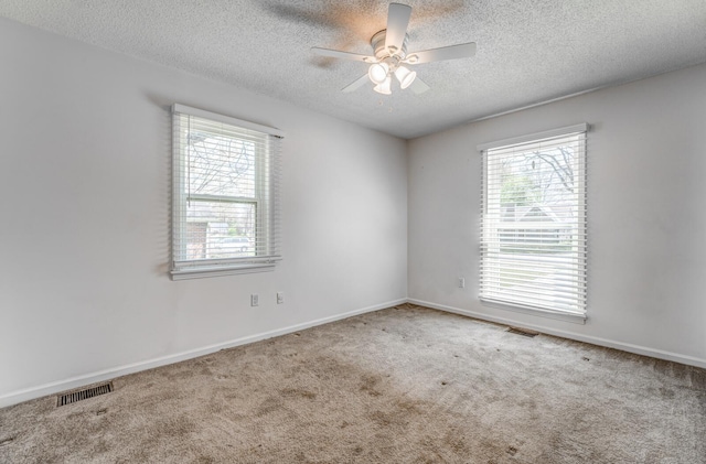 carpeted spare room featuring baseboards, a textured ceiling, visible vents, and a ceiling fan