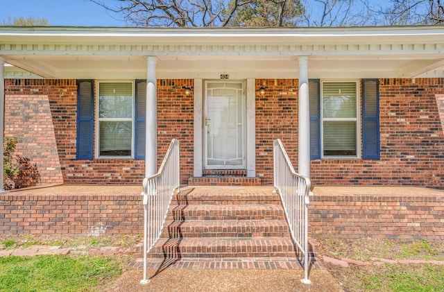 doorway to property featuring brick siding and a porch