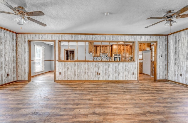 unfurnished living room with a textured ceiling, baseboards, ceiling fan, wood finished floors, and ornamental molding