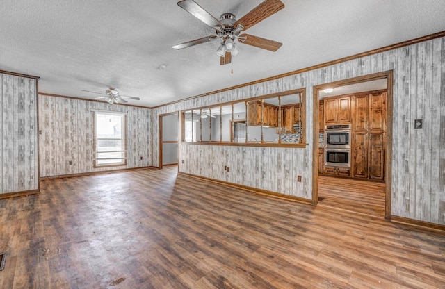 unfurnished living room with a textured ceiling, wood finished floors, ornamental molding, and a ceiling fan