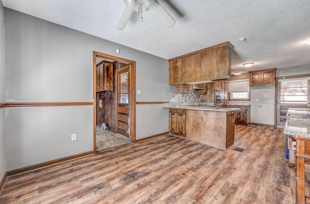 kitchen featuring a ceiling fan, wood finished floors, a peninsula, brown cabinets, and visible vents