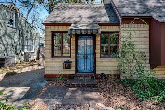 property entrance featuring fence, brick siding, and roof with shingles