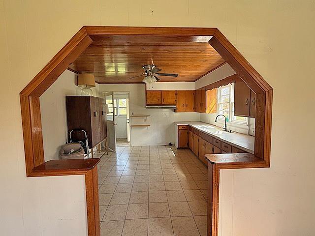 kitchen with light tile patterned flooring, wooden ceiling, a sink, brown cabinets, and ceiling fan