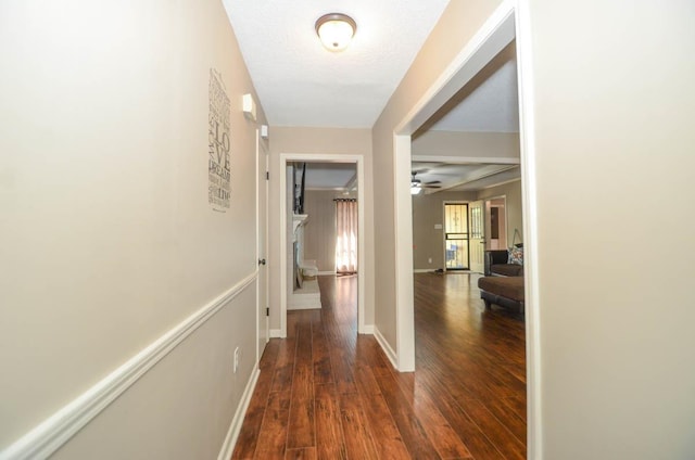 hallway with a textured ceiling, wood finished floors, and baseboards