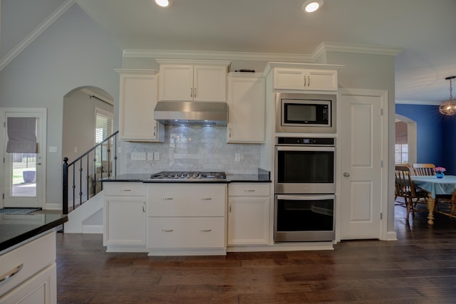 kitchen featuring exhaust hood, arched walkways, ornamental molding, dark countertops, and stainless steel appliances
