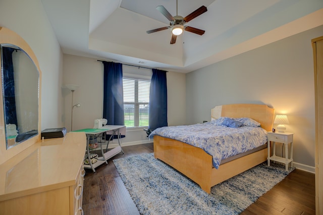bedroom featuring a tray ceiling, baseboards, a ceiling fan, and dark wood finished floors