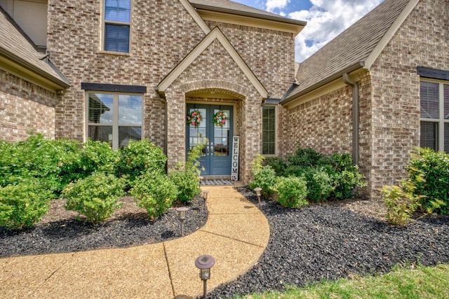 doorway to property with brick siding, french doors, and a shingled roof
