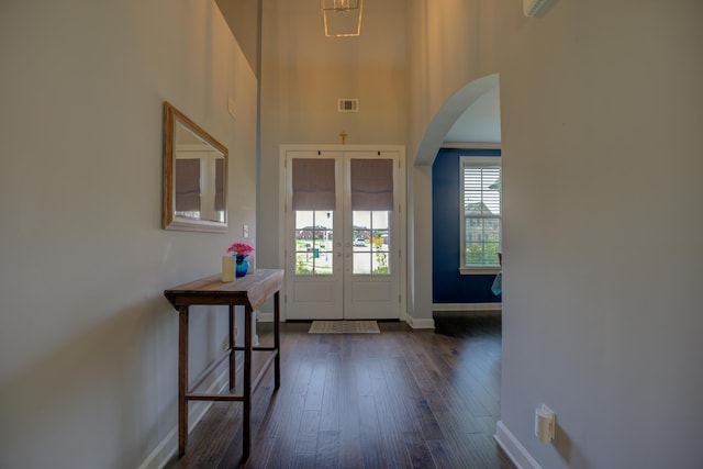 entryway featuring visible vents, arched walkways, dark wood finished floors, a towering ceiling, and french doors