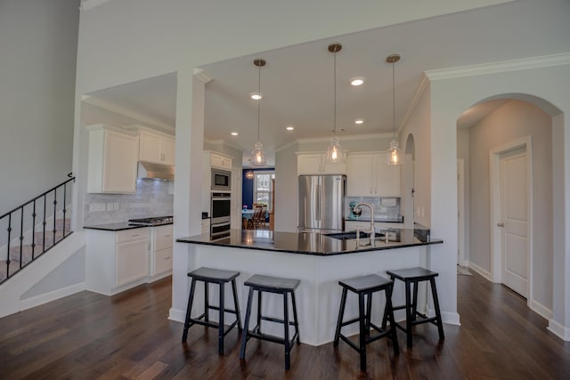 kitchen featuring arched walkways, appliances with stainless steel finishes, under cabinet range hood, a sink, and dark countertops