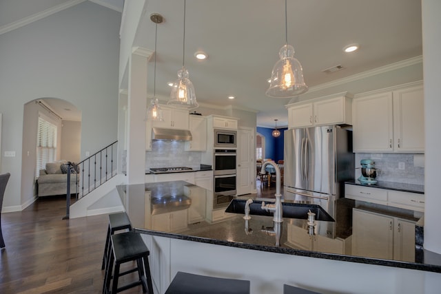 kitchen with arched walkways, a sink, ornamental molding, under cabinet range hood, and stainless steel appliances