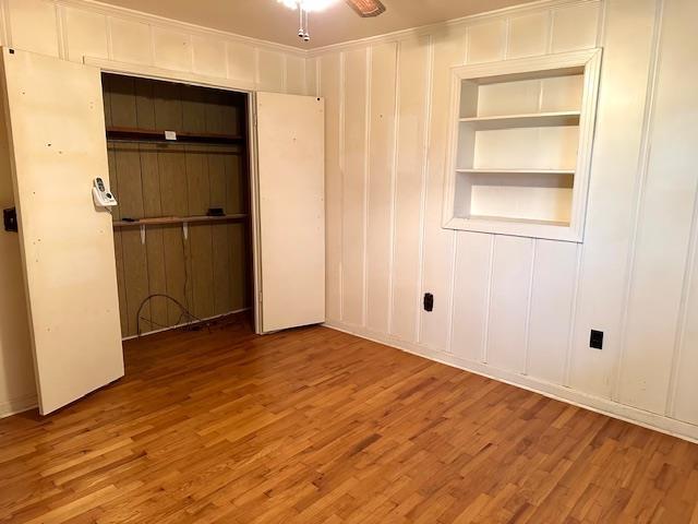spare room featuring built in features, wood finished floors, a ceiling fan, and a decorative wall