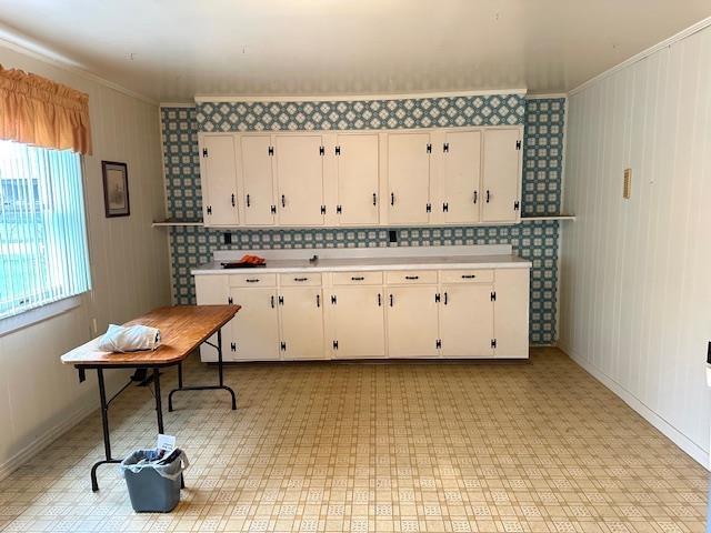 kitchen with baseboards, ornamental molding, light countertops, white cabinetry, and light floors