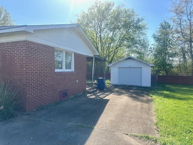 view of home's exterior with a detached garage, driveway, brick siding, an outbuilding, and a yard