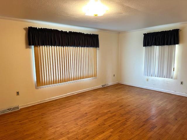 spare room with visible vents, baseboards, ornamental molding, a textured ceiling, and wood finished floors