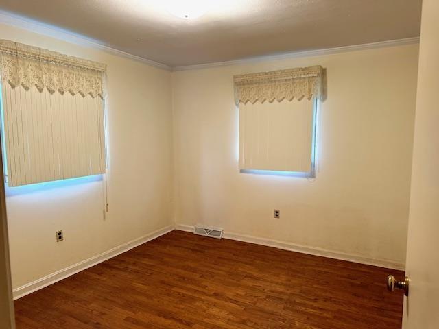 unfurnished room with visible vents, baseboards, crown molding, and wood finished floors