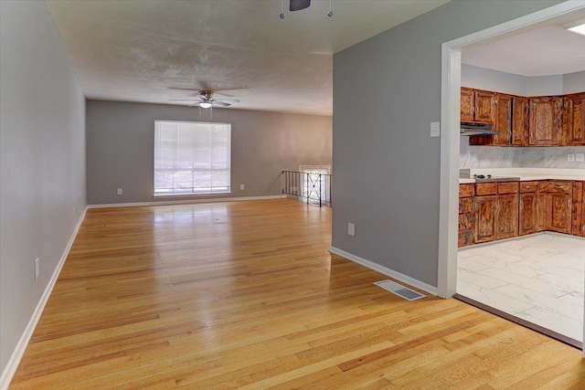interior space featuring baseboards, light wood-style flooring, a ceiling fan, under cabinet range hood, and visible vents