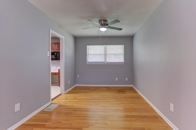 spare room with baseboards, a textured ceiling, light wood-style floors, visible vents, and ceiling fan