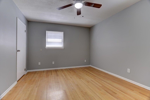 spare room with light wood-type flooring, ceiling fan, baseboards, and a textured ceiling