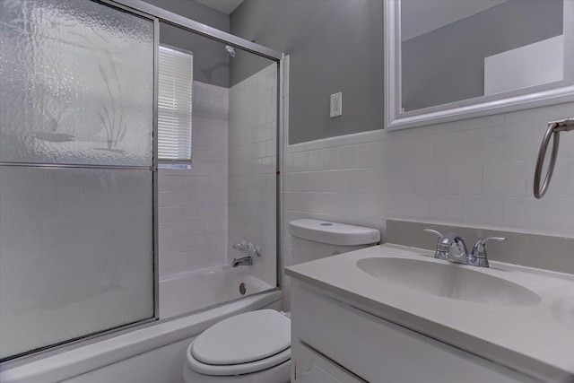 bathroom with toilet, enclosed tub / shower combo, vanity, and tile walls