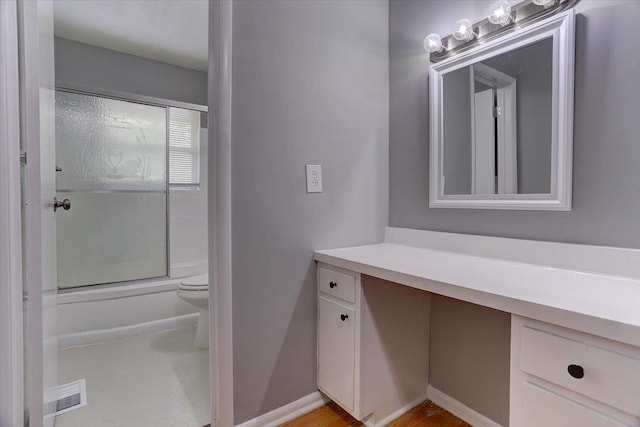 full bath with toilet, enclosed tub / shower combo, vanity, and baseboards