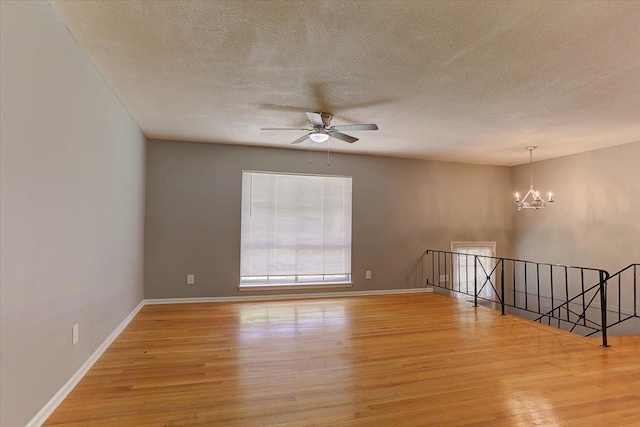 unfurnished room with light wood-style flooring, a textured ceiling, baseboards, and ceiling fan with notable chandelier
