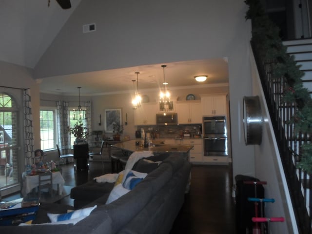 living area featuring crown molding, high vaulted ceiling, visible vents, stairway, and a notable chandelier