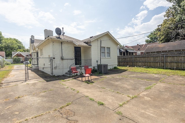 rear view of house featuring fence, central AC unit, a gate, and a chimney