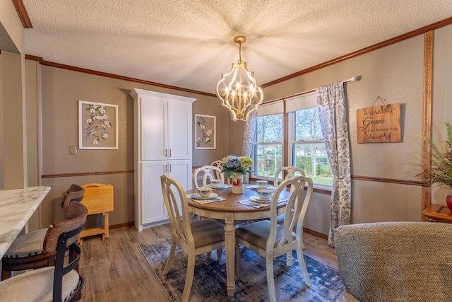 dining area with light wood-type flooring, a textured ceiling, an inviting chandelier, and ornamental molding