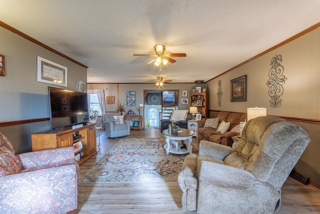 living room featuring a textured ceiling, wood finished floors, ornamental molding, and ceiling fan