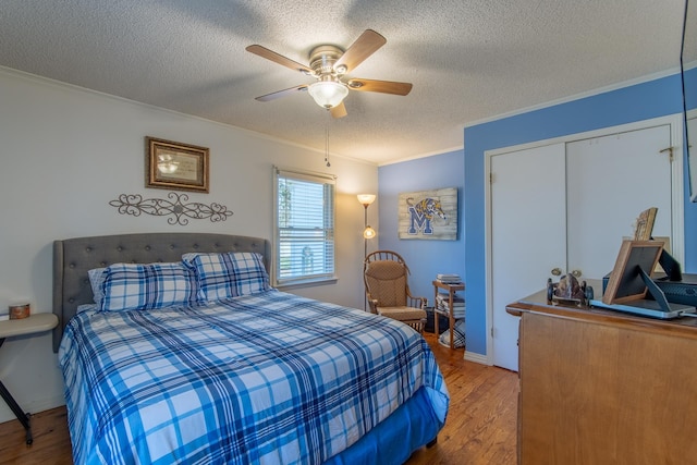 bedroom with a textured ceiling, a closet, a ceiling fan, ornamental molding, and wood finished floors
