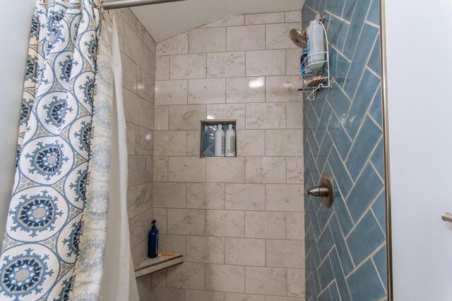 bathroom with a tile shower and lofted ceiling