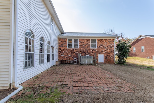 back of house featuring a patio area, brick siding, central air condition unit, and metal roof