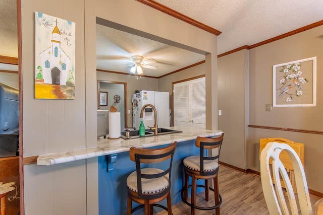 kitchen featuring a breakfast bar, white refrigerator with ice dispenser, a textured ceiling, crown molding, and wood finished floors