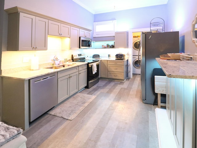 kitchen featuring stacked washer and dryer, ornamental molding, backsplash, stainless steel appliances, and a sink