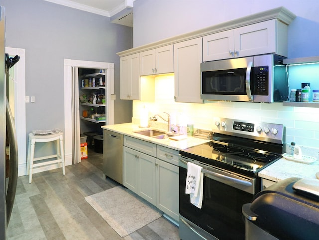 kitchen with tasteful backsplash, light wood-type flooring, ornamental molding, appliances with stainless steel finishes, and a sink