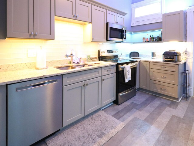 kitchen featuring open shelves, light stone counters, a sink, stainless steel appliances, and decorative backsplash