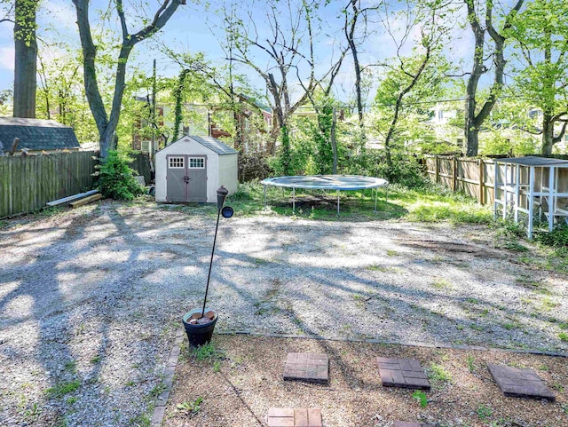 view of yard featuring a trampoline, a fenced backyard, a storage shed, and an outdoor structure