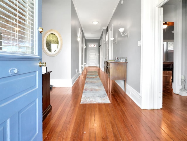 hallway featuring hardwood / wood-style floors, crown molding, and baseboards