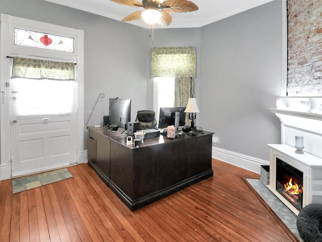 office space with a fireplace with flush hearth, baseboards, a ceiling fan, and wood finished floors