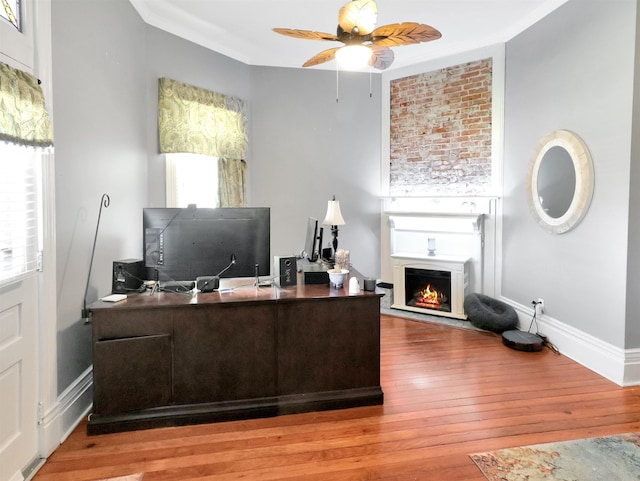 office space with hardwood / wood-style flooring, a lit fireplace, a ceiling fan, and crown molding