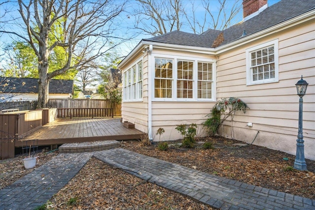 view of side of home with roof with shingles, a wooden deck, fence, and a chimney