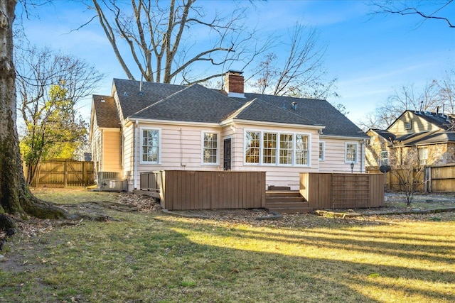 rear view of house featuring a chimney, cooling unit, a yard, fence, and a shingled roof