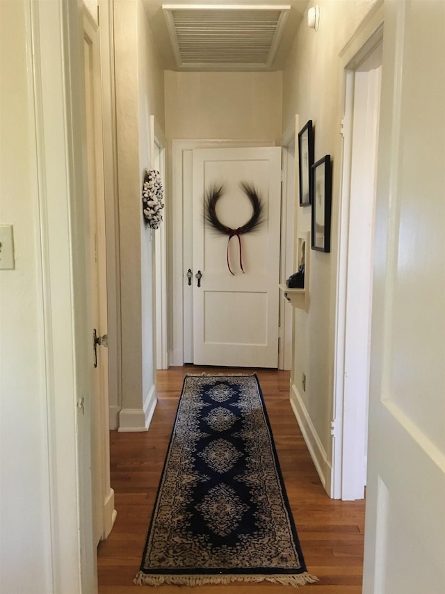 corridor with dark wood-type flooring, visible vents, and baseboards
