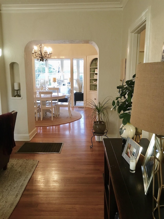 interior space featuring arched walkways, a notable chandelier, crown molding, and wood finished floors