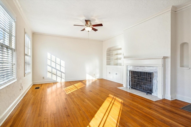 unfurnished living room featuring built in features, a fireplace, a ceiling fan, visible vents, and wood-type flooring