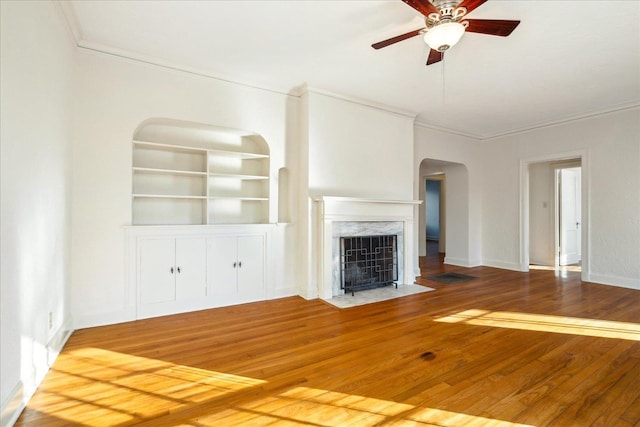 unfurnished living room featuring ornamental molding, a ceiling fan, hardwood / wood-style floors, arched walkways, and a high end fireplace