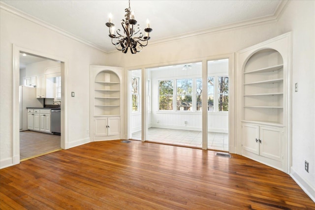 unfurnished dining area featuring crown molding, built in features, visible vents, hardwood / wood-style floors, and a notable chandelier